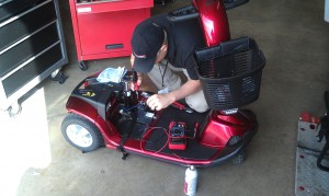 Male field technician working on a three-wheeled mobility scooter
